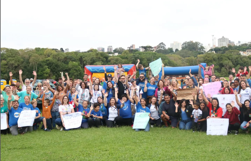Professora Amábile Marchi sorrindo com uma multidão de famílias da UPPA ao fundo